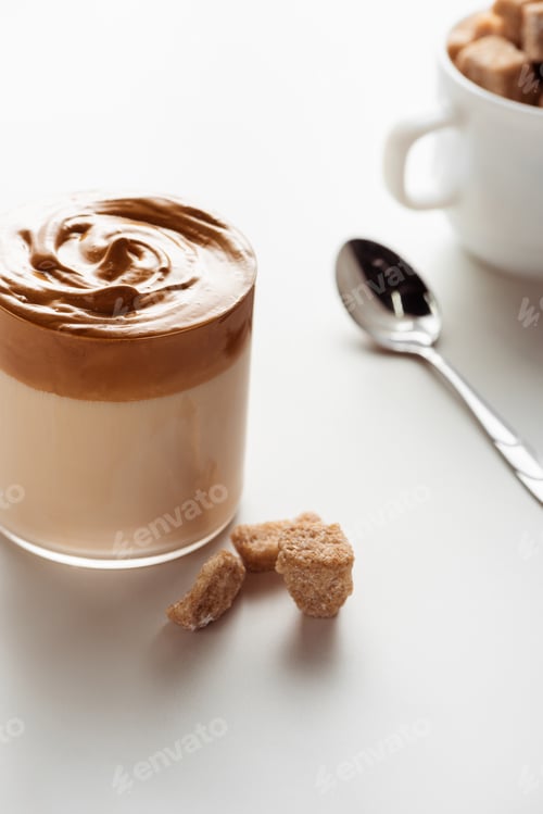 Preview: Selective Focus of Delicious Dalgona Coffee in Glass Near Spoon And Brown Sugar on White Background