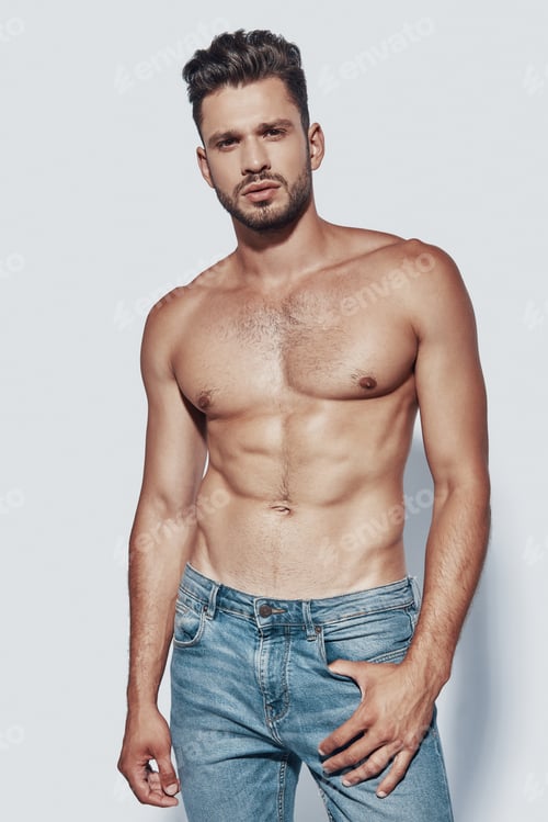 Preview: Handsome young shirtless man looking at camera while standing against grey background
