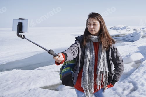 Preview: Female traveler outdoors at icy landscape using monopod to make selfie picture