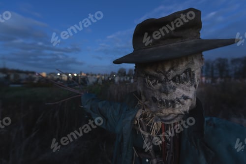 Preview: Terrible scarecrow in dark cloak and dirty hat stands alone on a cemetery