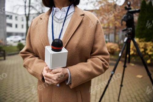Preview: A female journalist in a beige coat reports outdoors on a chilly autumn afternoon