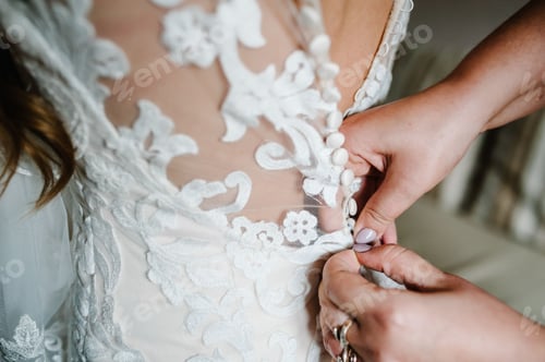 Preview: Bridesmaid helping bride fasten buttons on corset and getting her dress, preparing bride in morning