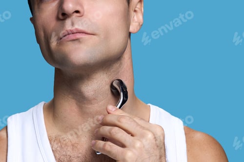 Preview: Caucasian Young Adult Man Using Facial Roller on Neck Against Blue Background
