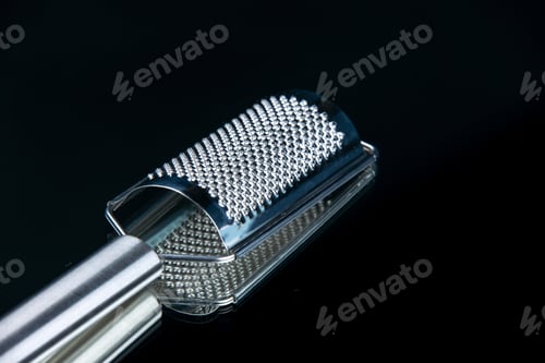 Preview: Vertical view of kitchen cheese grater lying on the right side on isolated black background with