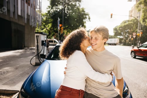 Preview: Couple kissing while charging their electric vehicle on a sunny day