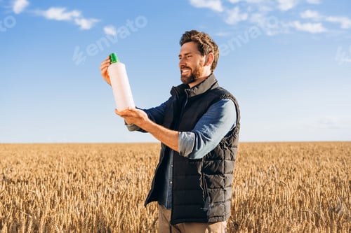 Preview: Farmer holding fertilizer bottle in wheat field smiling at sunset
