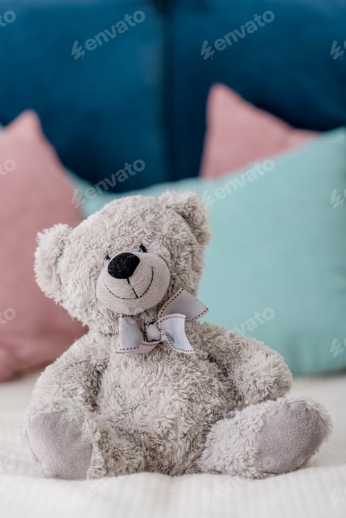 Preview: Close up vertical view of teddy bear sitting on the bed with pillows on background