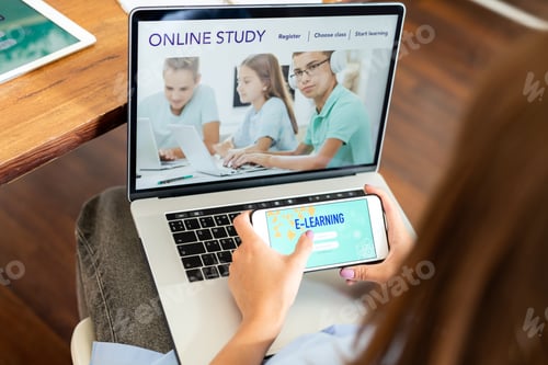 Preview: Young female student holding smartphone over laptop keypad