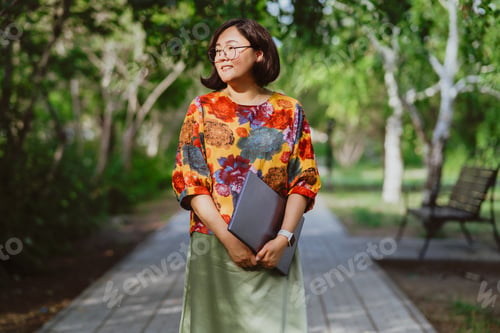 Preview: Confident young woman professional with a laptop in a vibrant city park