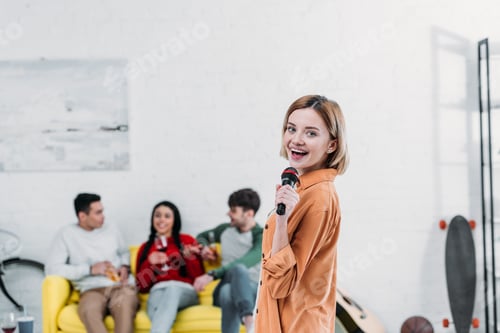 Preview: pretty girl singing karaoke while multiethnic friends enjoying drinks on yellow sofa