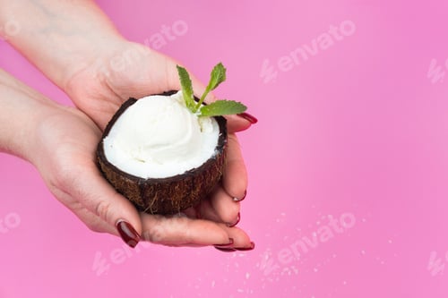 Preview: Vanilla ice cream balls in a fresh coconut half, decorated with mint leaves in your hand on a pink
