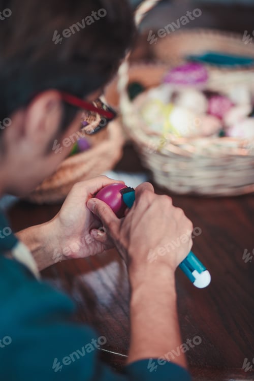Preview: Man decorating the Easter eggs by scratching patterns on dyed eggs