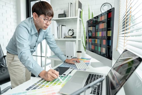Preview: Male graphic designer is standing to choosing color swatch samples on multiple screens and working