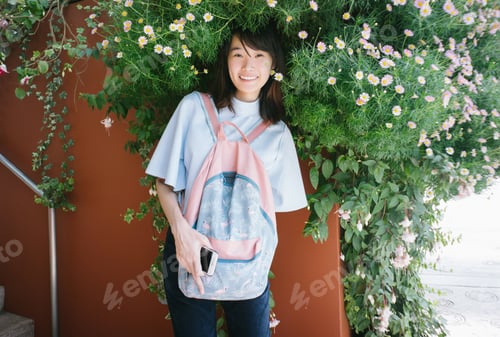 Preview: Asian woman wearing casual summer clothes with backpack looking at camera on flowers background