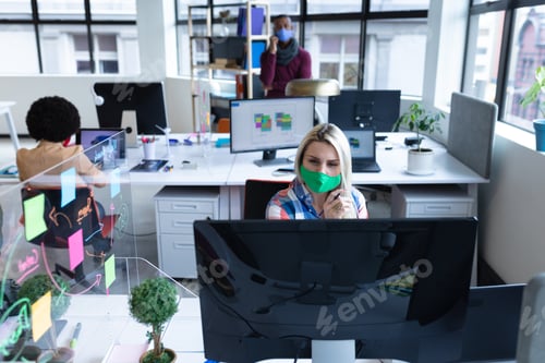 Preview: Caucasian businesswoman wearing face mask in creative office