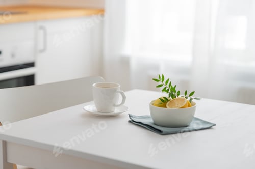 Preview: A cup of tea with lemon and a teapot on a white table against the background of a white kitchen