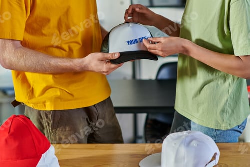 Preview: Cropped view of young african american designer holding printing layer near snapback while working