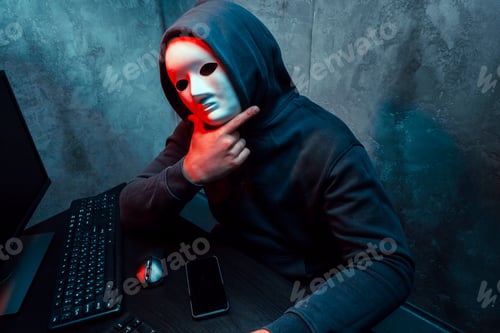 Vista previa: Hacker anónimo con máscara facial trabajando en una computadora en un cuarto oscuro