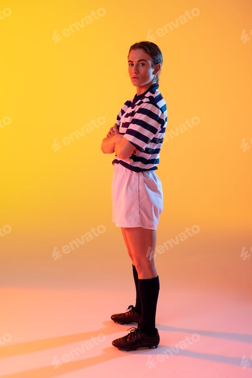 Preview: Portrait of caucasian female rugby player with arms crossed over neon yellow lighting