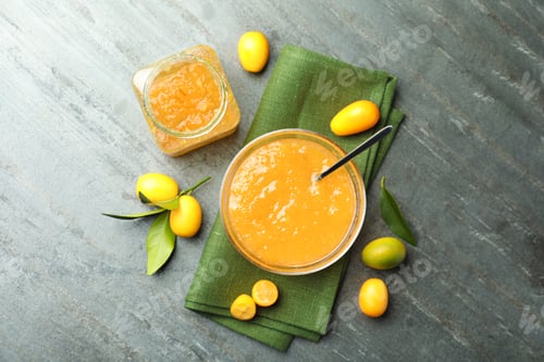 Preview: Delicious kumquat jam in bowl and fresh fruits on grey table, flat lay