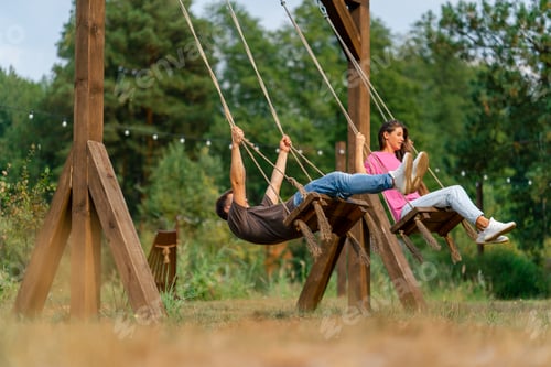 Preview: Loving couple man and girl riding on a large wooden swing overlooking a beautiful lake in nature