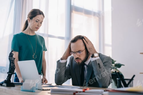 Preview: pensive lawyer and client at workplace with laptop and papers in office