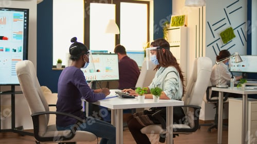 Preview: Multi ethnic employees with visor sitting at desk analysing statistics