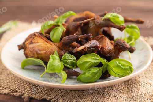 Preview: Smoked quails on a ceramic plate on a brown wooden background. Side view