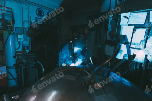Preview: Metalworker in welding mask soldering metal in forge workshop