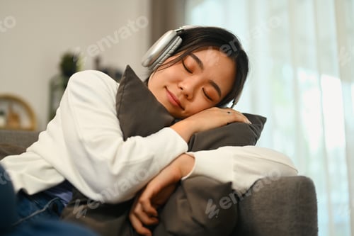 Preview: Peaceful young woman listening to music in headphone and sleeping on comfortable couch at home