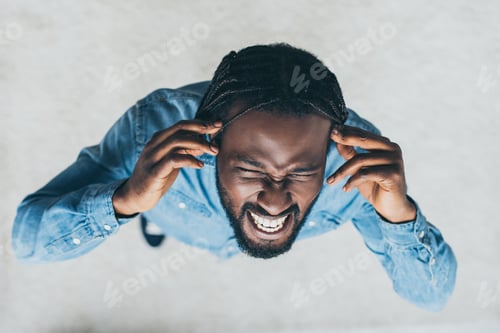 Preview: overhead view of african man holding hands near head while suffering from headache