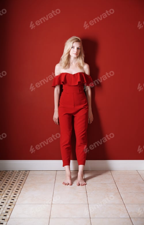 Preview: Beautiful young adult woman wearing red jumpsuit standing next to the wall