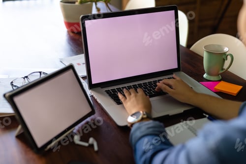 Preview: Hands of biracial woman using laptop and tablet with copy space on screen, working at home