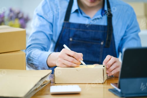 Preview: Start up small business owner writing address on cardboard box a.