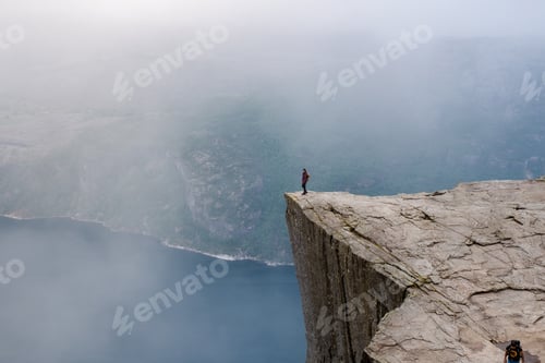 Preview: A lone hiker stands on the precipice of a dramatic cliff in Norway,Preikestolen, Norway