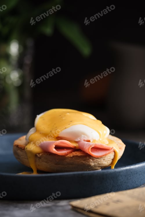 Preview: egg Benedict with hollandaise sauce on dark blue plate on table in kitchen