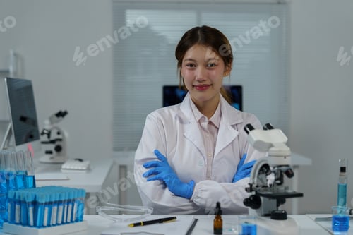 Preview: Smiling scientist in a lab coat and blue gloves, confidently crossing arms in a laboratory filled wi