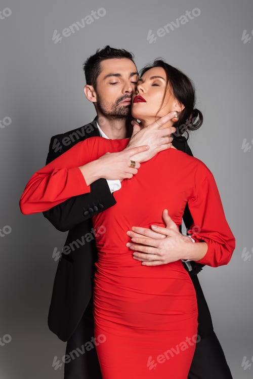 Preview: Passionate man touching neck of sexy girlfriend in dress on grey background