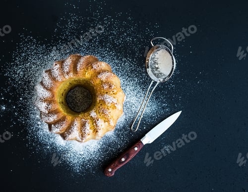 Vista previa: Bizcocho de yogur húmedo de naranja con azúcar en polvo en la parte superior, fondo grunge oscuro.