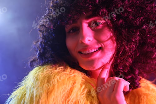 Preview: Beautiful young woman in yellow fur coat on color background in neon lights, closeup