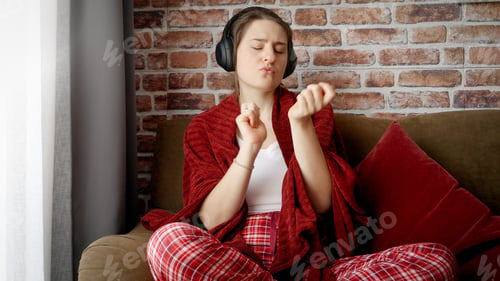 Preview: Happy smiling woman with headphones dancing on sofa in living room