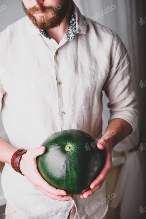 Preview: Bearded man in shirt holds in hands green watermelon