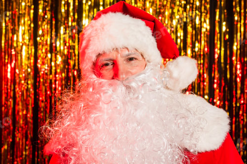 Preview: Portrait of bearded santa claus in hat looking at camera near blurred tinsel