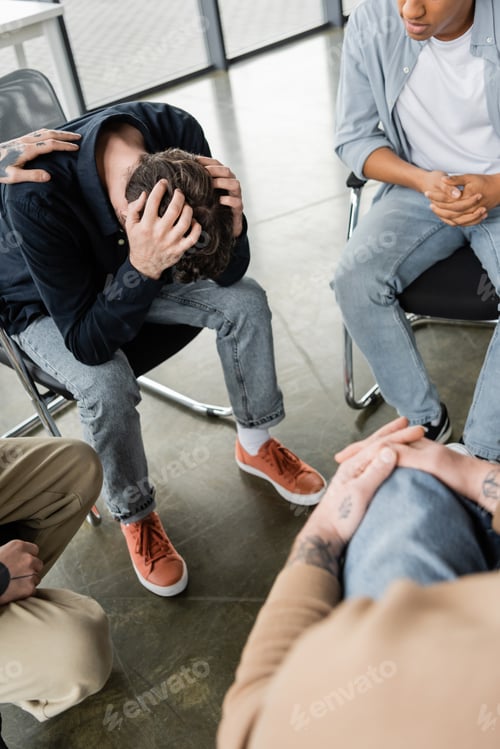 Preview: Interracial group calming depressed person with alcohol addiction in rehab center