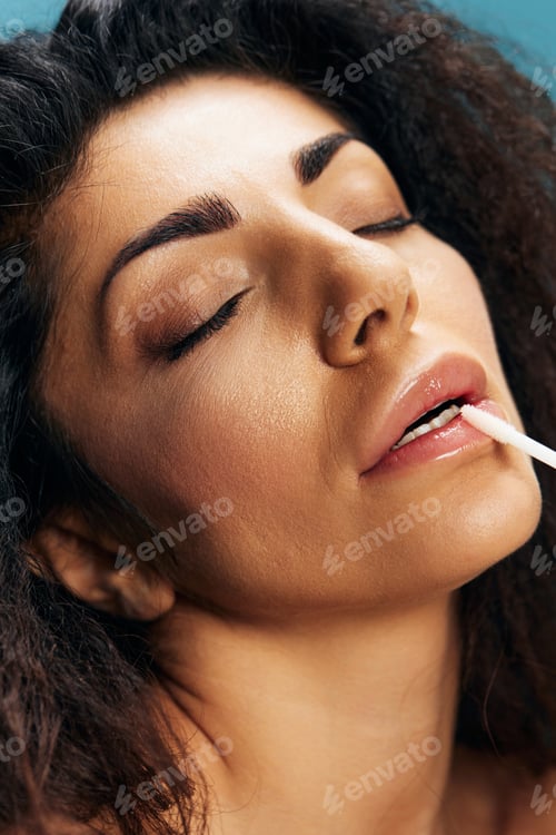 Preview: Lip Augmentation Concept. Pretty Tanned Curly Latin Woman Putting Lipstick Closing Eyes Over Blue