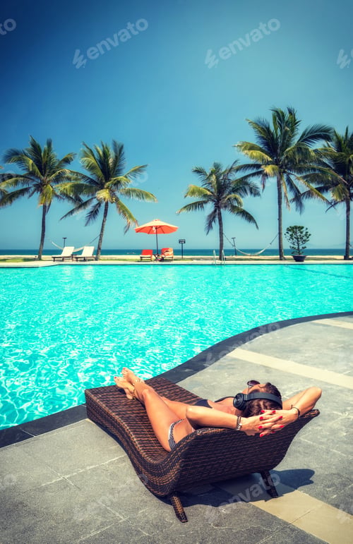 Preview: Woman at the swimming pool at the tropical resort with heaphones