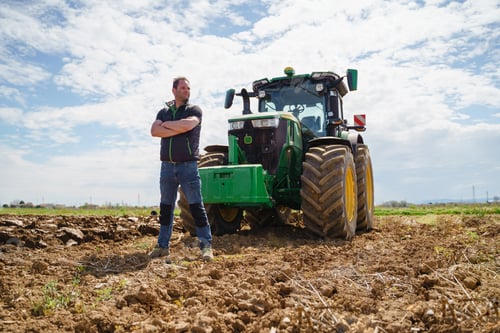 Preview: A skilled farmer proudly stands next to his plowing tractor, demonstrating his expertise in field