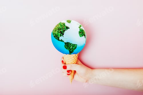 Preview: Female hand holding waffle cone with planet Earth model as ice cream dessert on pink background.