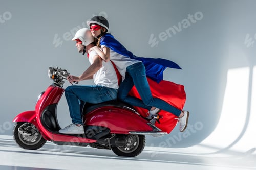 Preview: side view of couple in superhero costumes riding red scooter together