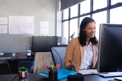 Preview: African American woman taking notes while viewing monitor with succulent on office desk, copy space